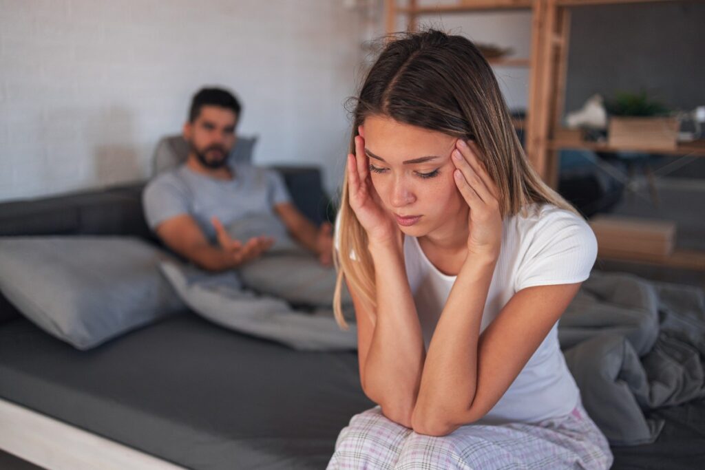A man and a woman sitting on a bed having an argument