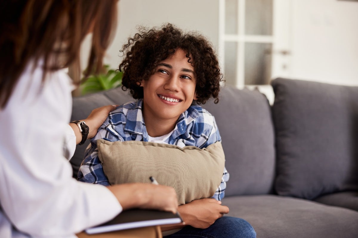 A teenage boy sitting on a couch smiling at his therapist in Naperville