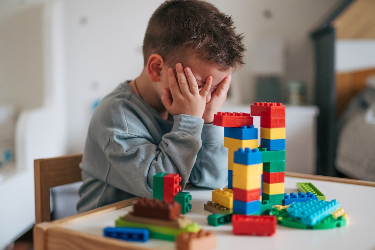 A child holding his head in frustration while playing with toy blocks