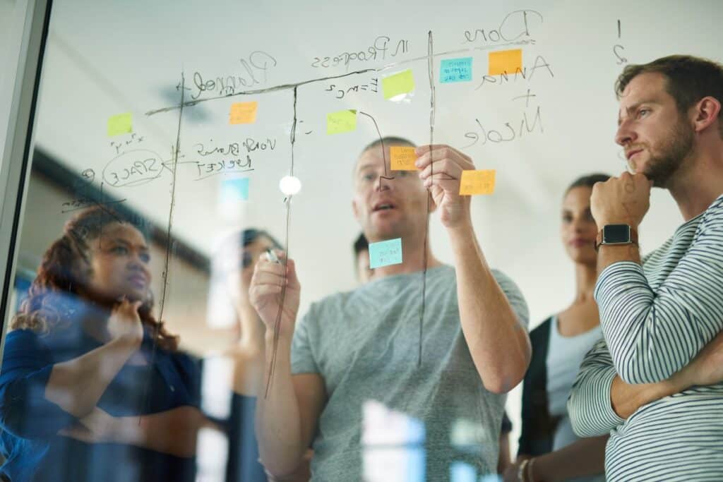 A group of coworkers reviewing a table of plans written on glass